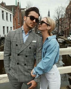 a man and woman standing next to each other in front of some buildings on the water