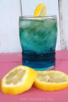 a glass filled with blue liquid next to two lemons