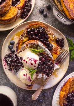 blueberry french toast with ice cream and berries on plates next to two cups of coffee