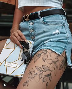 a woman with tattoos on her legs holding a notebook