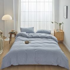 a bed with blue sheets and pillows in a white room next to a table with two lamps