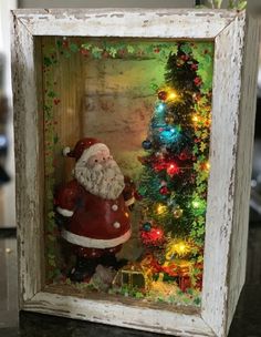 there is a small christmas decoration in a frame on the table next to a tree