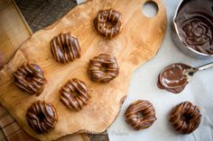 chocolate covered donuts sitting on top of a wooden cutting board next to some dipping sauce