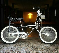 a white bicycle parked in front of a cross on a building with a light behind it