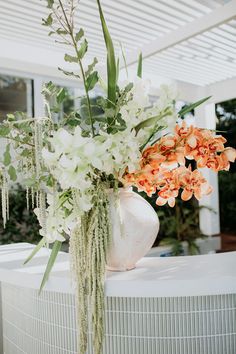 a vase filled with flowers sitting on top of a white counter next to a plant