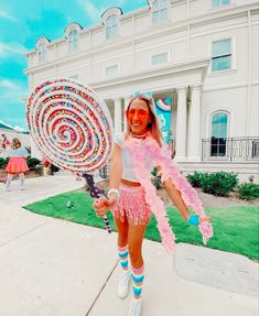 a woman in pink and white outfit holding a large lollipop on the sidewalk