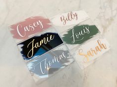 four stickers with names on them sitting on a marble countertop in front of a white wall