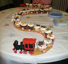 a table topped with cupcakes and a train on it's track shaped like the letter c