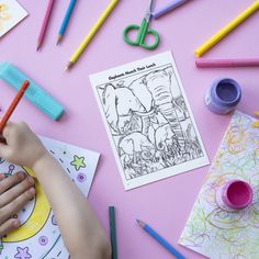 a child's hand holding a pencil while drawing on paper with colored crayons