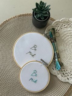 two cross stitch hoops sitting on top of a table next to a potted plant