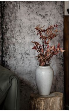 a white vase filled with flowers sitting on top of a wooden stump next to a wall