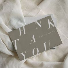 two thank you cards sitting on top of a white cloth covered bed sheet with the words, thank you