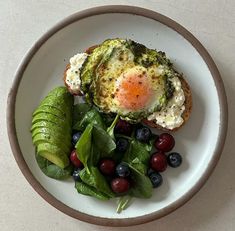 a white plate topped with an egg, spinach and blueberries next to a slice of avocado