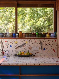 a bowl of fruit sitting on top of a counter next to a window with trees in the background