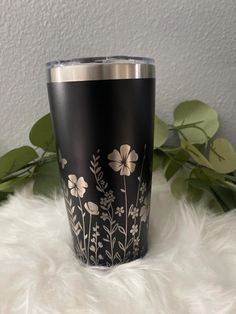 a black and silver tumbler sitting on top of a white fur covered floor next to plants