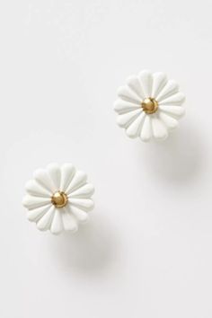 two white and gold flower shaped earrings on a white surface, one with a golden center