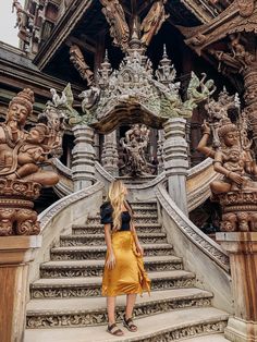 a woman standing in front of an ornate stair case with statues on the sides and steps leading up to it