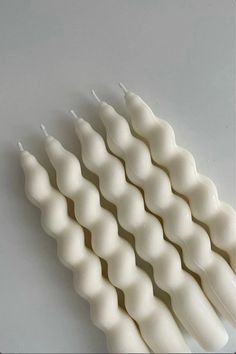 four white candles are lined up on a gray surface, with one candle in the shape of a zigzag