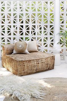 a wicker couch sitting on top of a white rug in front of a wooden trellis