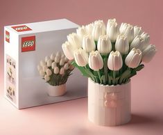 white tulips in a vase next to a lego box on a pink background