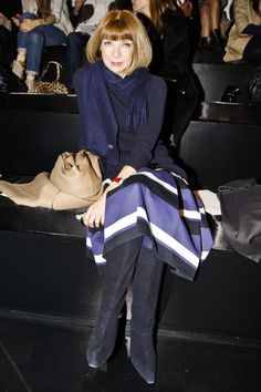 a woman sitting on a bench in front of a group of people at a fashion show