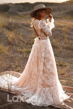 a woman in a long dress and hat standing on a desert plain looking at the horizon