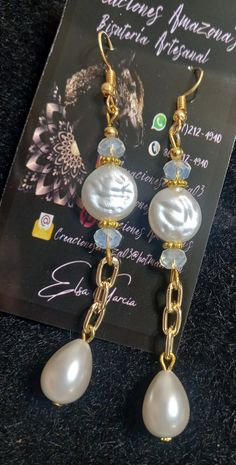 two white pearls and gold chain earrings on top of a black carpeted floor next to a card