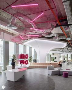 the inside of an office building with pink and white accents on the ceiling, couches and tables in front of large windows