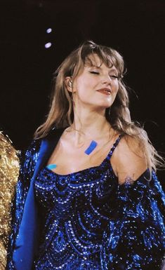 a woman in a blue dress standing next to a gold jacket on her shoulders and looking off into the distance