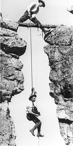 two men are hanging from ropes on the rocks