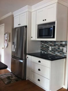 a kitchen with white cabinets and black counter tops, stainless steel refrigerator and microwave oven