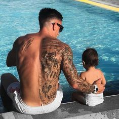 a man sitting next to a little boy near a swimming pool with tattoos on his back