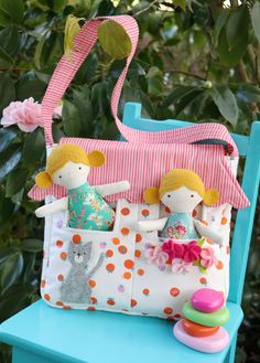 two dolls sitting on top of a blue chair next to a pink and white purse