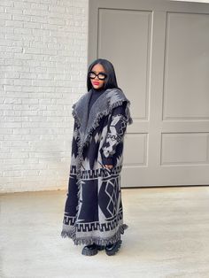 a woman standing in front of a garage door wearing a black and white coat with an animal print pattern