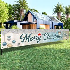 a merry christmas sign in front of a house with holiday decorations on the grass and trees