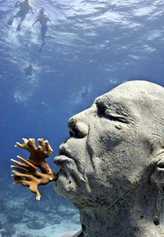 an underwater sculpture of a man with corals in his mouth