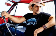 a man wearing a cowboy hat sitting in the driver's seat of a red truck