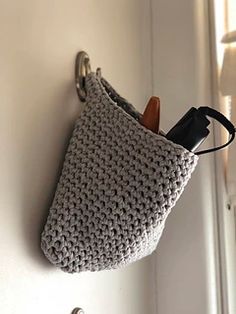 a crocheted purse hanging on the wall next to a hook with a pair of scissors in it