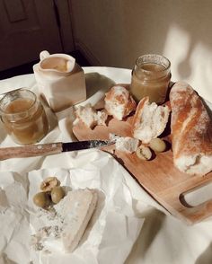 bread and olives on a wooden cutting board with jars of honey in the background