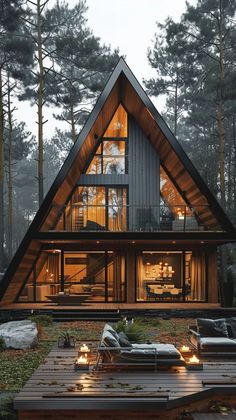 a large wooden house in the woods with lights on it's windows and patio furniture