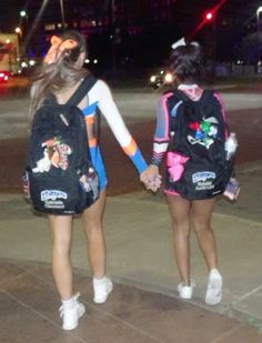 two girls are walking down the sidewalk holding hands and wearing backpacks with cartoon characters on them