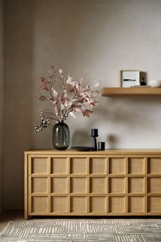 a vase filled with flowers sitting on top of a wooden cabinet next to a shelf