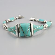 a bracelet with turquoise stones and silver beads on it's sides, sitting on a gray surface