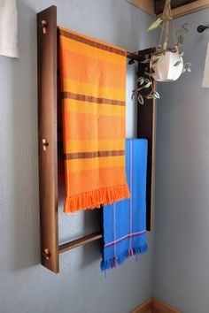 a towel rack with two towels hanging from it's sides and a potted plant in the corner