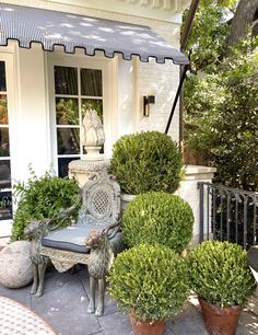 a bench sitting on top of a sidewalk next to potted plants and bushes in front of a house