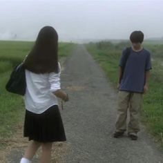 two children are standing on the side of a road in front of an open field