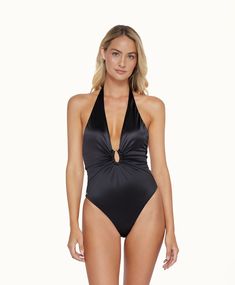 A blonde woman wearing a black one piece swimsuit stands in front of a white wall. Party V-neck Stretch Swimwear, Luxury V-neck Swimwear For Poolside, Adjustable Straps V-neck Swimwear For Pool, V-neck Stretch Swimwear For Poolside, Luxe Swimwear, Jumpsuit Coverup, Wedding Guest Accessories, Black Nylon V-neck Swimwear, Halter Style