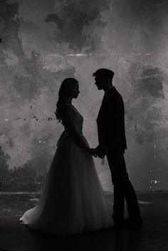 a man and woman standing next to each other in front of a wall with graffiti