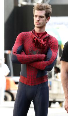 a man in a spiderman costume standing next to another man with his arms crossed