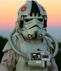 a man in a star wars helmet with a radio on his chest and the sun setting behind him